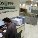 Pakistani government office worker processing NSER registration documents with computer, official BISP signage visible, organ